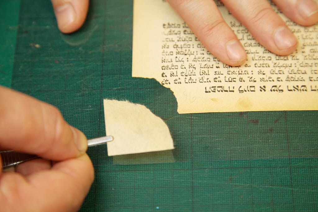 Torn page corner being repaired by toned Japanese tissue