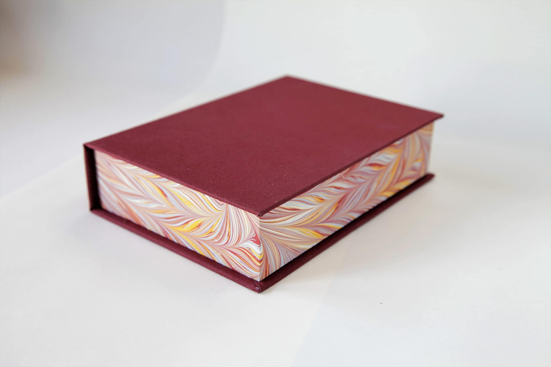 Clamshell book box closed with maroon cover and marbled edges on a white background