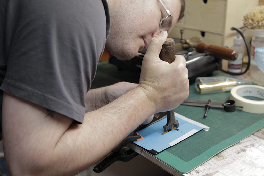 Bookbinder using hot brass tool to add gold decoration to book cover